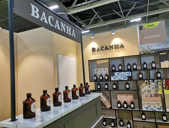 Stand Bacanha dans un salon professionnel, présentant des bouteilles et coffrets de sirops sur un comptoir et des étagères.