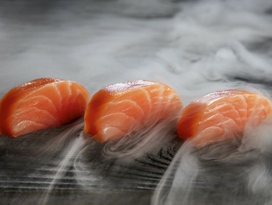Trois médaillons de saumon délicatement posés sur une surface sombre, enveloppés d’un léger nuage de fumée. La texture brillante du poisson contraste avec les volutes, créant une ambiance raffinée et sensorielle.