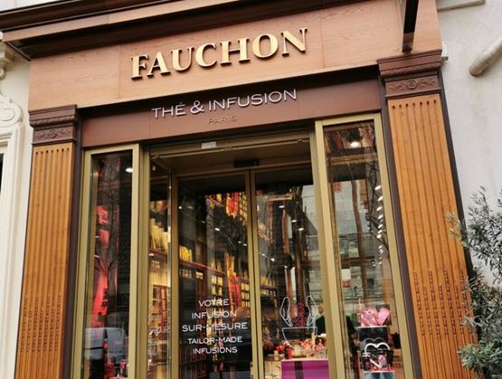 Façade de la boutique Fauchon « Thé & Infusion » à Paris, avec son enseigne dorée et ses vitrines élégamment agencées. À l’intérieur, des rayons bien garnis laissent entrevoir une sélection raffinée de thés, infusions et cadeaux gourmands.