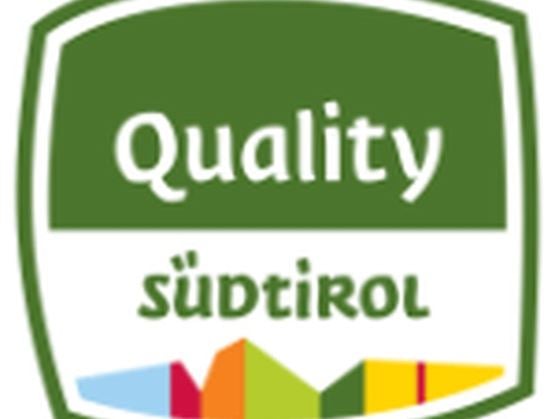 Logo "Quality Südtirol" sur fond vert avec une représentation stylisée et colorée des montagnes du Tyrol du Sud en bas de l’image.