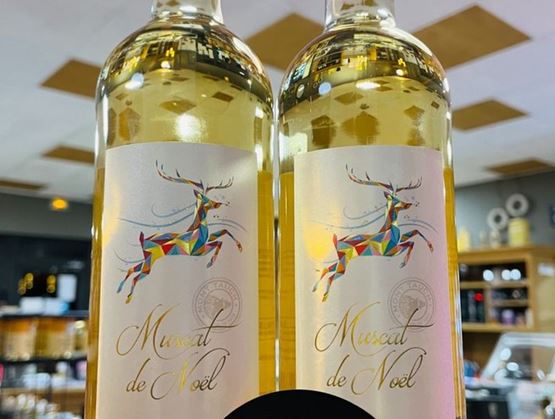 Deux bouteilles de Muscat de Noël avec une étiquette festive représentant un renne stylisé aux couleurs vives, exposées dans une boutique spécialisée.