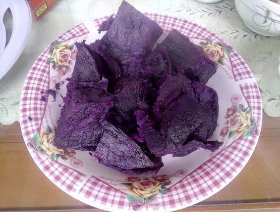 Assiette fleurie remplie de morceaux de gâteau violet foncé philippin appelé "munthul", présentée sur une table avec nappe transparente.