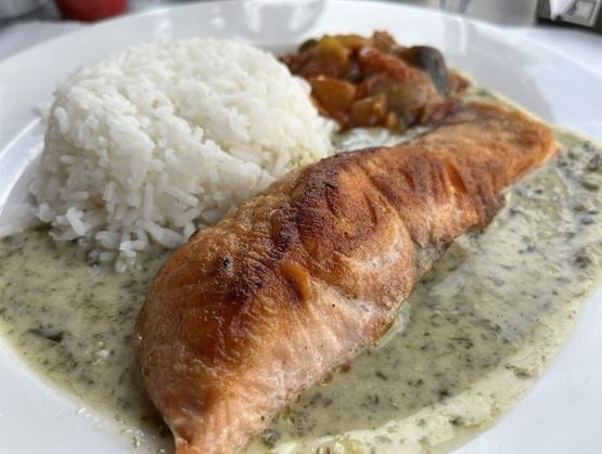 Assiette garnie d’un filet de saumon grillé nappé de sauce à l’oseille, accompagné de riz blanc et d’un mélange de légumes en sauce, servie dans un restaurant.