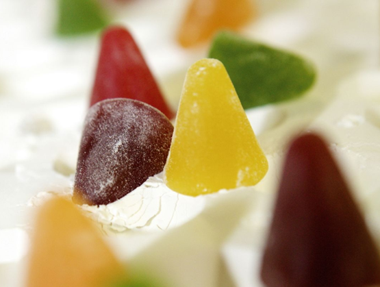 Close-up of colorful cuberdons, traditional Belgian cone-shaped candies, in various shades (yellow, red, green, orange) with a glossy, lightly powdered texture, arranged on a white background.