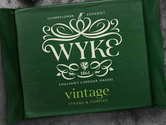 Emballage vert foncé d’un cheddar "Vintage" de la marque Wyke Farms, originaire de Champflower dans le Somerset (Angleterre). Le design raffiné met en avant le nom "WYKE" avec des ornements blancs élégants, ainsi que la mention "England’s Cheddar Makers – Since 1861". L’inscription "Vintage – Strong & Complex" indique un fromage affiné à la saveur prononcée et complexe. Le packaging évoque tradition, savoir-faire et qualité artisanale britannique.