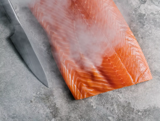 Filet de saumon frais légèrement fumant, posé sur une surface en pierre grise, avec un couteau de cuisine en acier à côté.