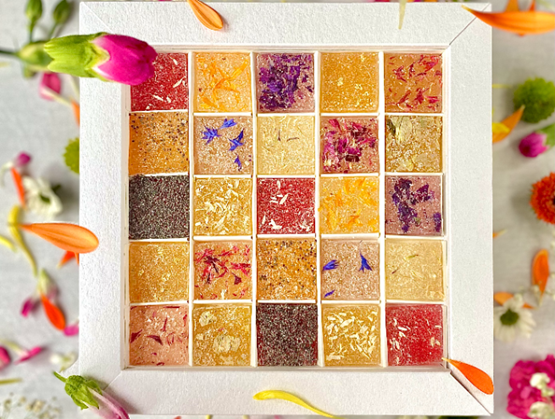 Coffret Inflorescence de Fleurs de Chocolats, composé de pâtes de fleurs artisanales aux couleurs et parfums variés, présenté dans un écrin blanc décoré de pétales.