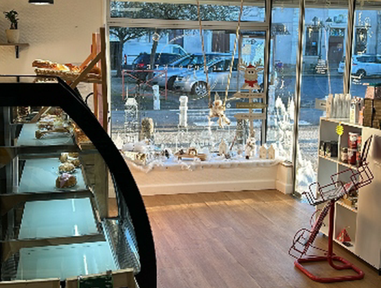 Intérieur d’une épicerie fine avec vitrine réfrigérée, rayonnages de produits et décorations blanches en vitrine.