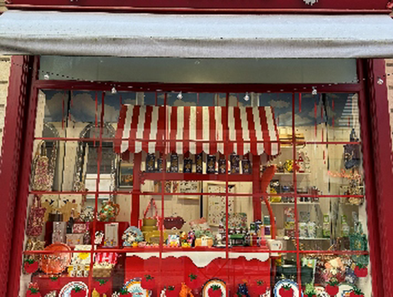 Façade rouge de la boutique La Ferme, avec une vitrine décorée de produits d’épicerie et d’objets artisanaux.