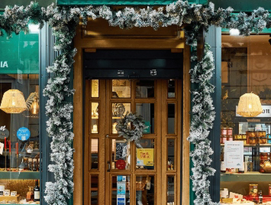 Façade décorée d’une épicerie fine Comptoir Gourmand, avec une entrée en bois encadrée de guirlandes hivernales.