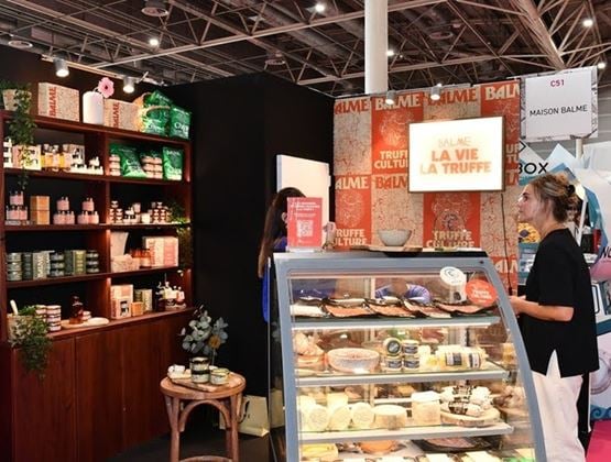 Exhibition stand showcasing truffle-based products, featuring a refrigerated display case, stocked shelves, and visitors.