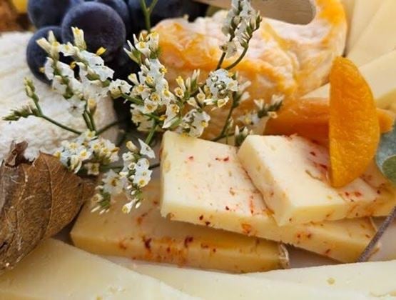 Assorted cheese platter garnished with flowers, dried fruits, and black grapes.