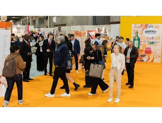 Visitors walking through the aisles of a trade show dedicated to gourmet food products, featuring colorful exhibitor stands.