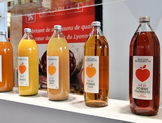 Bouteilles de jus de fruits artisanaux exposées sur une étagère lors d’un salon professionnel.