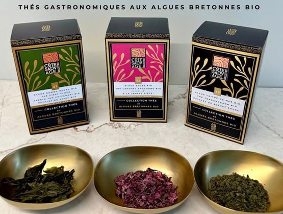 Trois boîtes de thés gastronomiques aux algues bretonnes bio sont présentées avec trois bols contenant des feuilles de thé et des algues séchées.