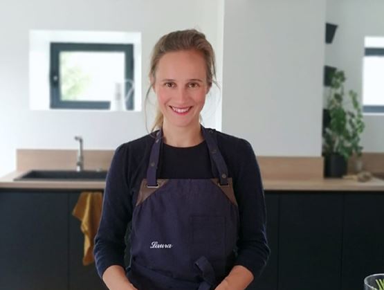 Portrait de Laura Huard, souriante en tablier, dans une cuisine lumineuse.