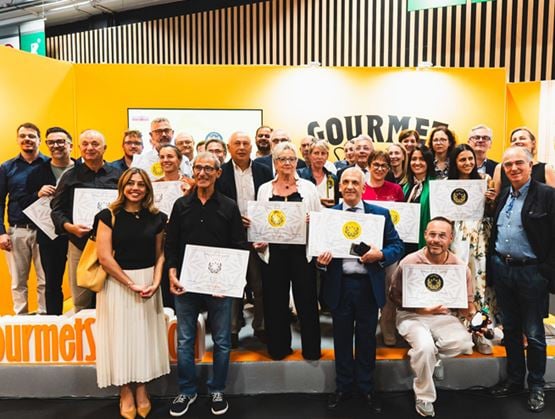 Photo de groupe des lauréats et participants du concours Gourmet Selection, tenant leurs diplômes devant le stand du salon.