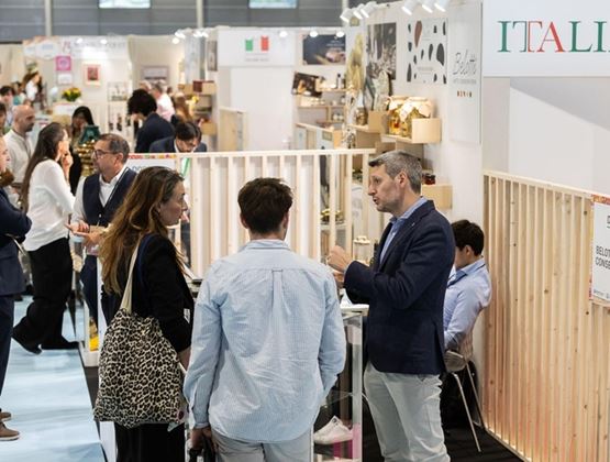 Visiteurs et exposants échangent sur des stands italiens lors d’un salon professionnel, avec une signalétique « ITALIA » visible au-dessus des espaces d’exposition.