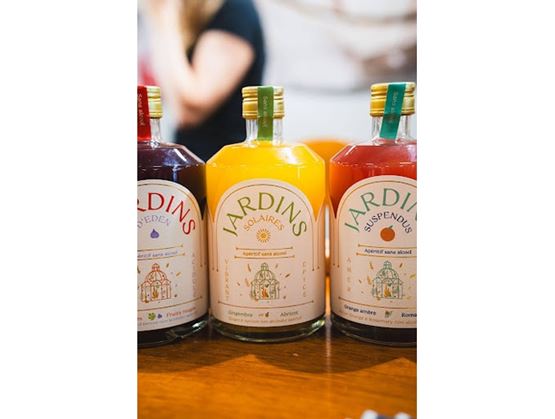 Three bottles of Jardins non-alcoholic aperitifs, in red, yellow, and orange hues, displayed on a table.