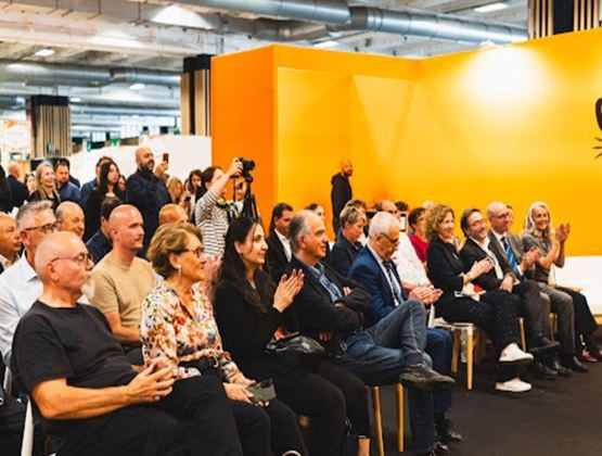 Public assistant à une conférence professionnelle sur un salon, applaissant face à une scène jaune.