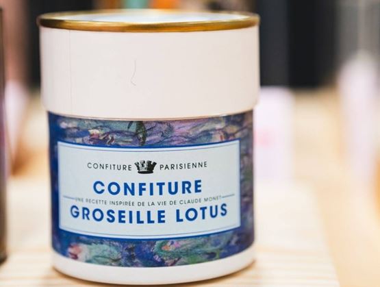 Close-up of a jar of Confiture Parisienne "Lotus Redcurrant" jam displayed on a wooden stand.