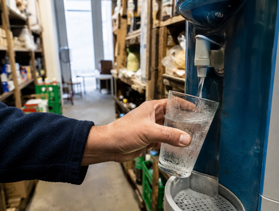 Une personne remplit un verre d’eau à un distributeur installé dans la réserve d’un commerce.