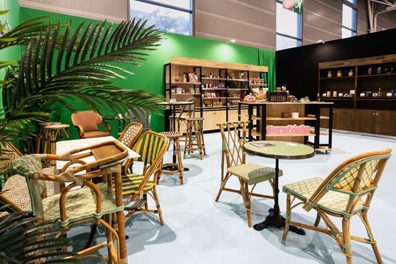 Espace boutique du salon Gourmet Selection : fauteuils en rotin, tables bistrot et étagères en bois garnies de produits d’épicerie.
