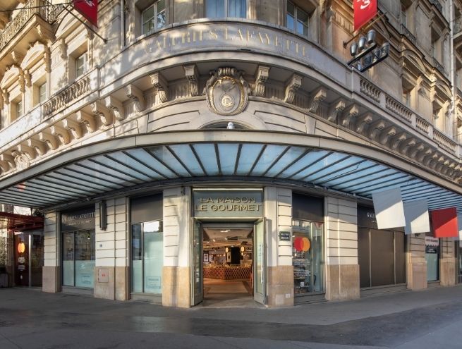 Entrée de La Maison Le Gourmet aux Galeries Lafayette, avec façade haussmannienne et marquise vitrée.