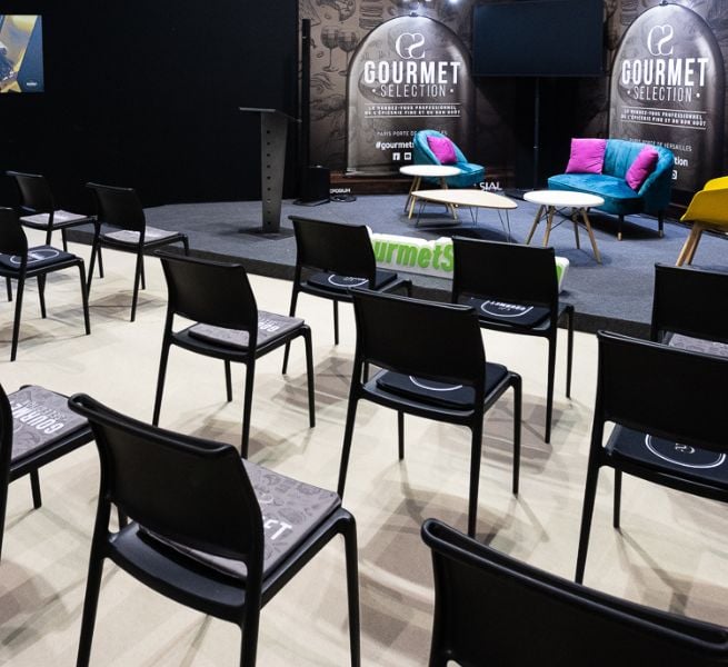 Conference area at the Gourmet Selection show with black chairs, a stage, and colorful furniture.