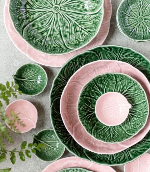 Set of glazed ceramic plates and bowls shaped like green and pink leaves, artistically arranged on a tabletop.