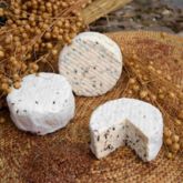 Trois petits fromages Bray au lin posés sur un tapis de paille, dont un entamé, avec des graines dorées en arrière-plan.