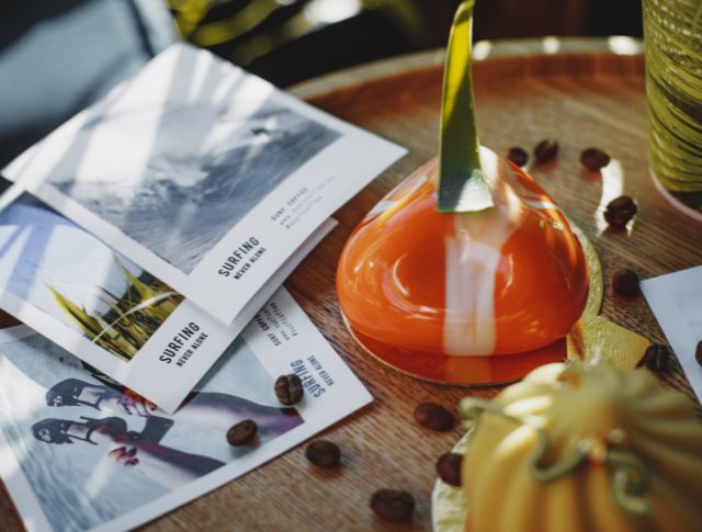 Gros plan sur un dessert coloré posé sur une table, accompagné de prospectus de surf et de grains de café.