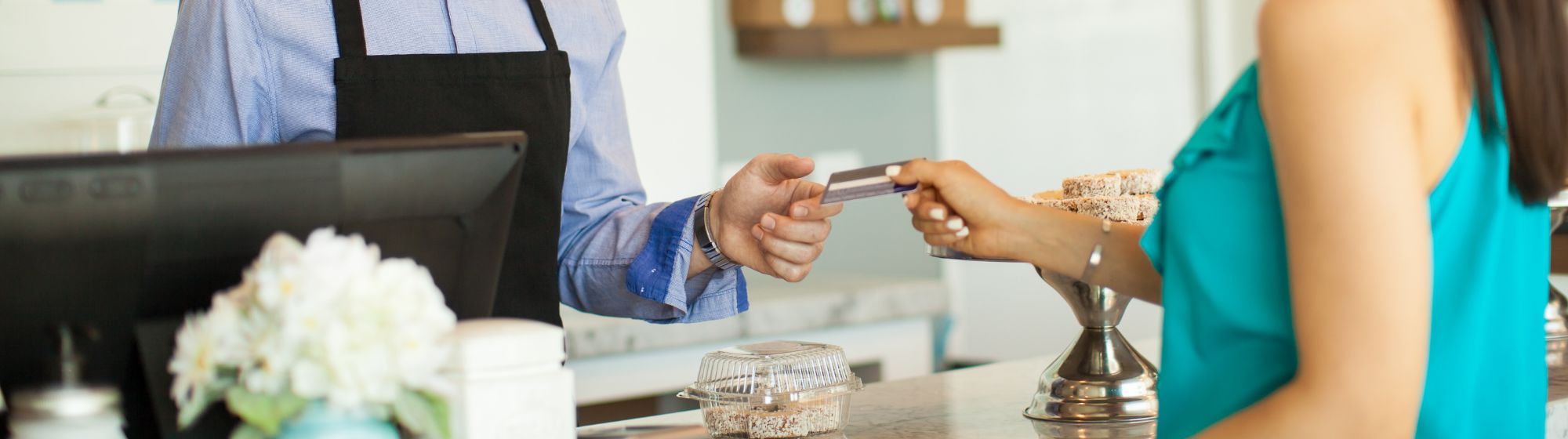 Customer handing a credit card to a shopkeeper behind a retail counter.