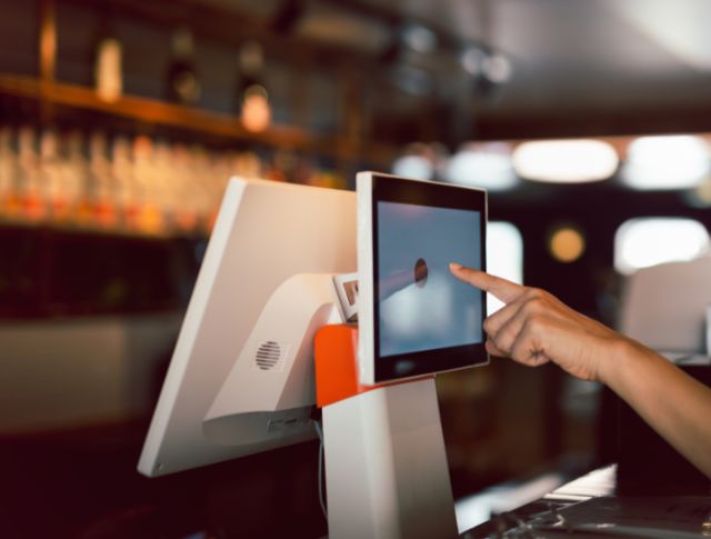 Main touchant un écran tactile de caisse dans un bar ou restaurant moderne.