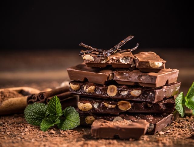 Pile de tablettes de chocolat aux noisettes entières, décorées de vanille et de menthe fraîche.