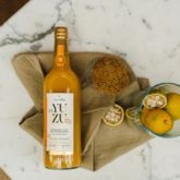 Alain Milliat yuzu juice bottle on a cloth with fruits and grains on a marble table.