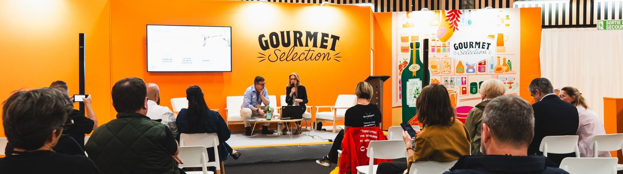 Conférence sur le salon Gourmet Selection, avec un public face à deux intervenants sur scène dans un espace aux couleurs orange.