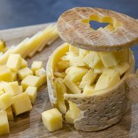 Fromage à pâte pressée coupé en dés et en lamelles, présenté dans une meule ouverte sur une planche en bois.