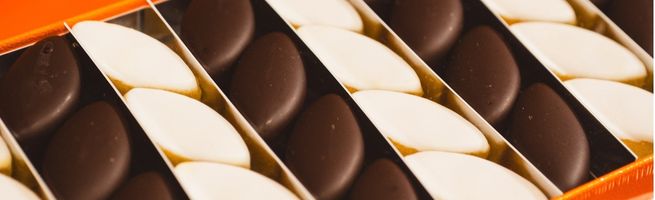 Assortiment de chocolats noirs et blancs alignés dans une boîte de présentation.