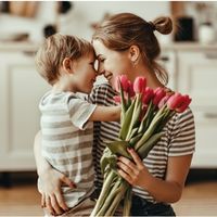 Personne tenant un bouquet de tulipes roses tout en portant un jeune enfant dans un intérieur chaleureux.