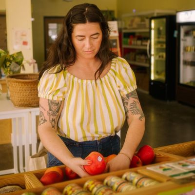 A person selecting fresh produce and jarred goods at a neighborhood grocery store, highlighting the shopping experience and product selection.