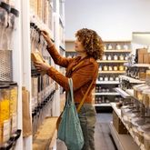 Client consultant des distributeurs de produits en vrac dans une épicerie spécialisée proposant une large sélection d’ingrédients et de références alimentaires.