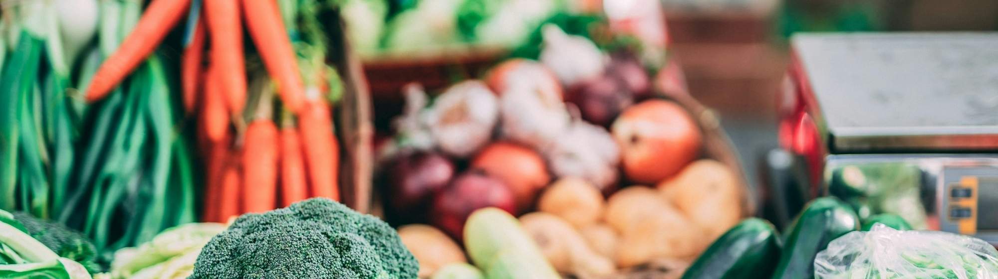 Fresh vegetable stall at a market with broccoli, carrots, onions, potatoes, and zucchinis