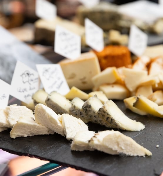 Assortiment de fromages découpés et présentés sur une ardoise avec étiquettes en fromagerie.