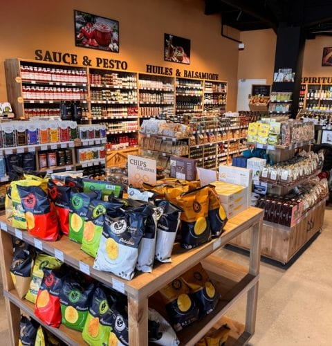 Intérieur chaleureux de l'épicerie Bottega Bastiano, avec des étagères garnies de sauces, pesto et produits italiens.