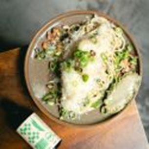 Bowl of creamy risotto topped with grated cheese, fresh herbs and mushrooms on wooden table.