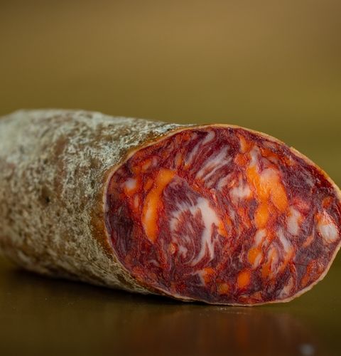 Sliced dry sausage with red and orange marbling, shown in close-up against a dark background.