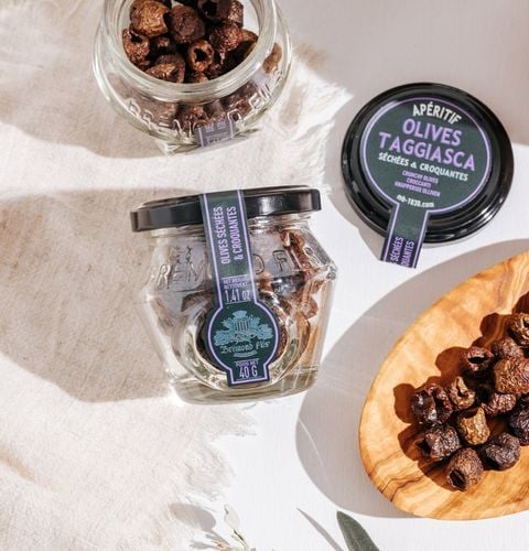 Bocaux d’olives Taggiasca séchées et croquantes, présentés avec olives dans une coupelle en bois.