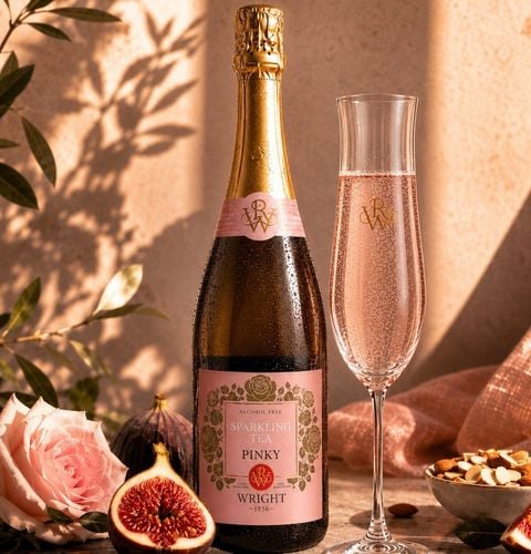 Bouteille de thé pétillant sans alcool rosé et flûte remplie, entourées de figues, amandes et rose dans une lumière douce.
