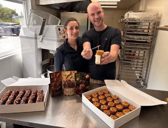 Deux pâtissiers souriants présentent des desserts et un pot de caramel dans une cuisine professionnelle